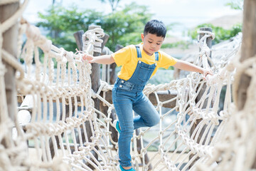Portrait of little boy playing on rope net bridge at the playground. Asian little boy walking and...