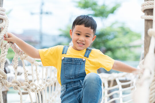 Portrait of little boy playing on rope net bridge at the playground. Asian little boy walking and climbing on rope bridge at the adventure rope park