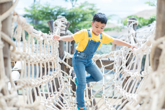 Portrait of little boy playing on rope net bridge at the playground. Asian little boy walking and climbing on rope bridge at the adventure rope park - Powered by Adobe