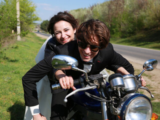 Fototapeta na wymiar Unusial wedding on the motocycle. the bride in a leather jacket, the groom in glasses. Happy couple smiling outdoors