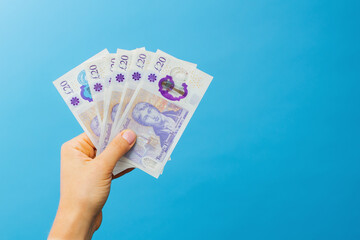 Image woman's hands which holds British pounds in her hands isolated over blue studio background