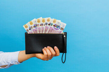 Female hands holding british pounds banknotes in black wallet on a blue background. - obrazy, fototapety, plakaty