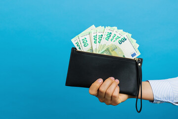 Female hands holding black wallet with euro banknotes on a blue background