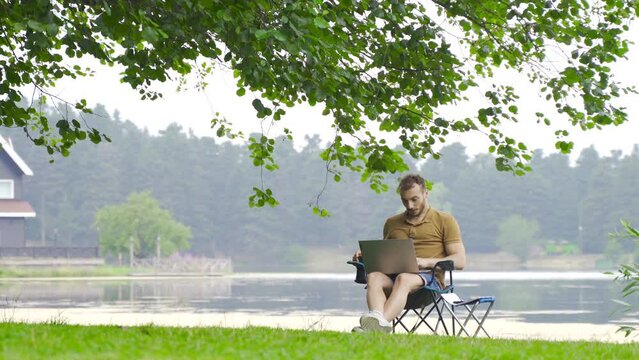 Man working with computer by lake in nature.
Man looking at laptop happy and rejoicing working in nature.
