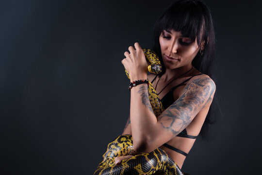 Photo of brunette woman holding anaconda in shadows