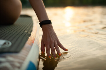 A girl rides a Sap Ford during sunset. Hand close-up in the water.