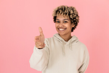 Blurry African American imitating shooting in studio. Female model with curly hair pointing finger gun at camera. Portrait, studio shot, fun concept