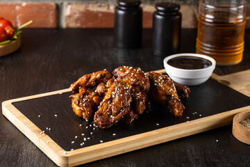 Grilled teriyaki chicken wings with sesame on dark cutting board on dark wooden background