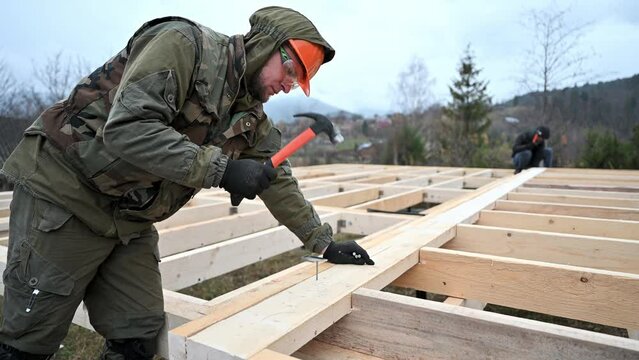 Man worker building wooden frame house on pile foundation. Carpenter hammering nail into wooden joist, using hammer. Carpentry concept.