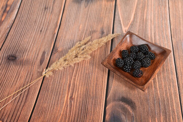 Ripe blackberries in a wooden bowl on a light wood background. Photo of blackberries in a bowl on a wooden table. A high-resolution product.