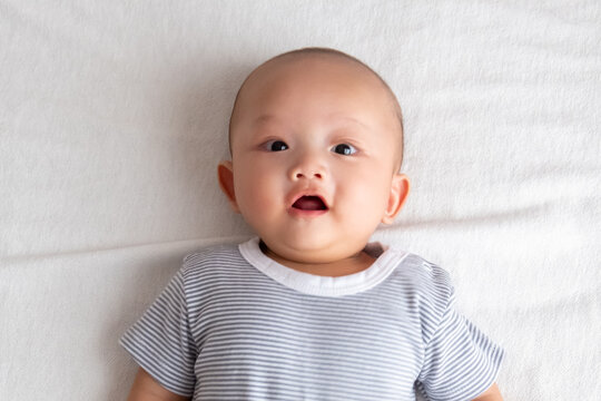 baby boy with big eyes smiling with mouth open on the white mattress