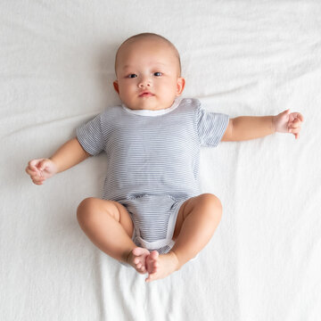 Top view is a baby boy wearing a striped shirt. Lie with your legs up and your arms outstretched on the bed.