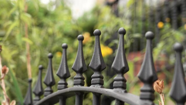 Wrought pointed metal fence black spikes with linear perspective in green garden. Protection and security concept