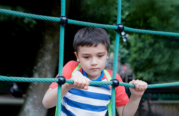 Portrait Kid holding robe in outdoors playground, Child climbing adventure park on sunny day  Spring or sSmmer, Lonely young boy playing alone in public playground.