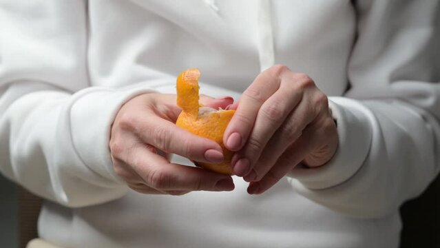 Girl hands peel ripe tangerine. Person holding mandarin and removes orange peel