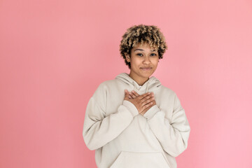 Charming African American woman in studio. Female model in hoodie making cute face and hugging herself. Portrait, emotion concept