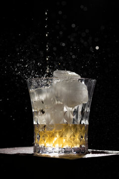 Isolated photo of whiskey with splashes on ice cubes and on black background. Small drops around the splash. Image with selective focus.