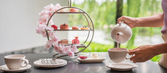 Woman hand pouring hot tea with Afternoon tea set and Pink dessert at luxury hotel