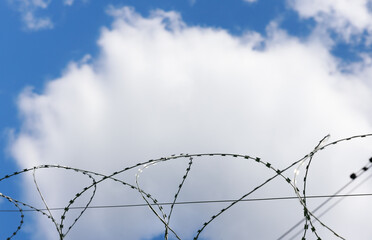 barbed wire as a restriction . Against the backdrop of a bright blue sky with clouds. High quality photo