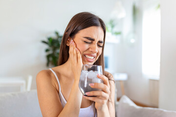 Young woman with sensitive teeth and hand holding glass of cold water with ice. Healthcare concept....