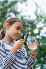 The child examines the water with a magnifying glass. Selective focus.