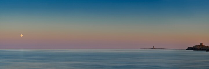 Sunset over Meditteranean sea in Menorca with lighthouse and full moon