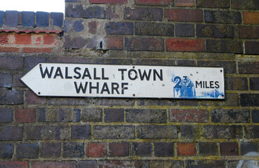 Fototapeta na wymiar Old Metal Distance Sign on Brick Wall beside Canal 'Walsall Town Wharf' 