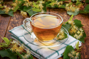 linden flowers on a wooden board and a glass transparent mug of fragrant tea. concept of home healing medicine