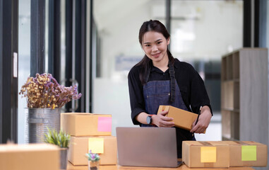 Young attractive asian woman owner startup business look at camera work happy with box at home...
