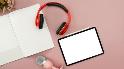 Flat lay digital tablet, wireless headphone and microphone on pink background. Radio, podcasts, blogging and technology concept