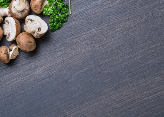 Brown colored edible mushrooms or cremini mushrooms on black table with herbs. Top view.