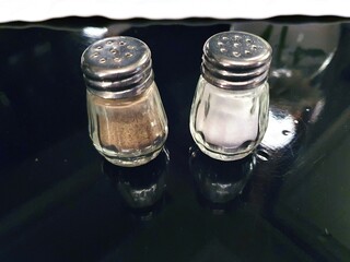 Salt and pepper in jars on a stylish black lacquered surface. Salt and pepper shakers.
