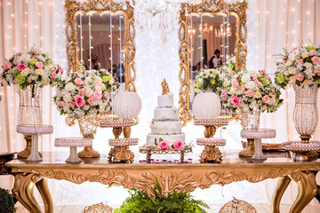 a table decorated with flowers and sweets and a white wedding cake decorated with roses and a golden biscuit wedding couple on top