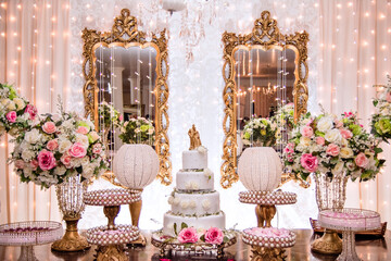 a table decorated with flowers and sweets and a white wedding cake decorated with roses and a golden biscuit wedding couple on top