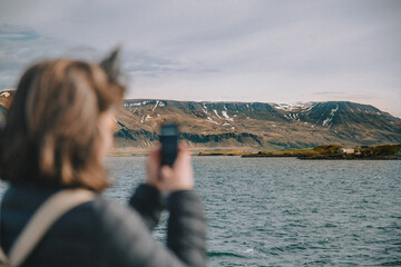 Woman taking photograph on iPhone in front of mountains and sea