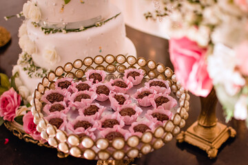 trays with sweets, brigadeiros in pink molds, flowers and a cake in the background
