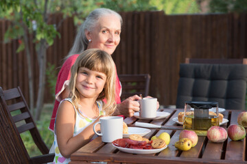 family lunch in the garden near the house on a summer day. an elderly woman with an adult daughter and grandchildren at a birthday table