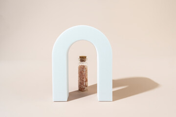Two glass bottles with pink sea salt for spa procedures for face or body standing between geometric forms