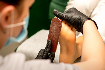 Pedicurist rubbing heel with a special grater on pedicure treatment in a beauty salon
