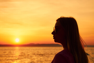 Close-up silhouette in profile of a woman in sunglasses, in the rays of the setting sun on the sea