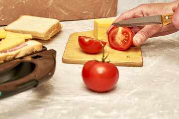a man making sandwiches in a sandwich maker cuts tomatoes on a cutting board