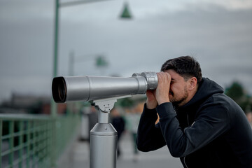 Fototapeta na wymiar a man in the evening in the city looks at the sights with large binoculars