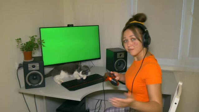Gamer girl welcomes the viewer to play with her on joysticks in game. Chromakey on computer screen. She plays the game. Video with a chroma key on the screen to insert any video or image.