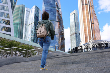 Fototapeta premium Woman goes up the stairs towards the skyscrapers of Moscow city. International business center in russian capital