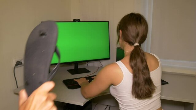 Girl is typing text on the keyboard then guy hits her with slipper. Chromakey on computer screen. She is frightened by the guy but shows him a fist. Video with a chroma key on the screen to insert an