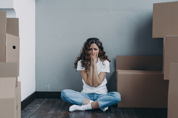 Sad tired girl feels stress due to moving, divorce or eviction sitting in room with cardboard boxes - obrazy, fototapety, plakaty