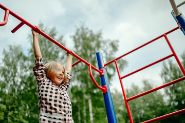 Obraz premium the girl is hanging on a horizontal bar on the playground, the child is engaged in sports