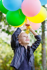 Joyful happy emotional laughing little girl standing with many colorful balloons in  park, birthday celebration, vertical
