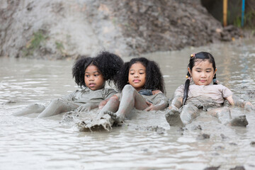 Group of happy children girl laying and playing in wet mud puddle on summer day