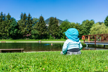 A baby sits with sun protective clothing at a lake in summer